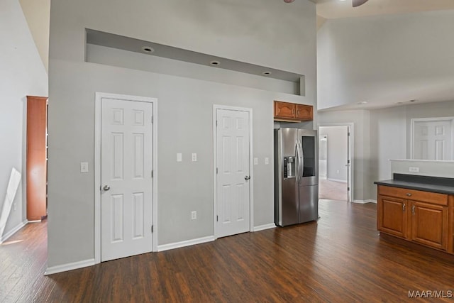 kitchen featuring a towering ceiling, stainless steel refrigerator with ice dispenser, dark wood-type flooring, and ceiling fan