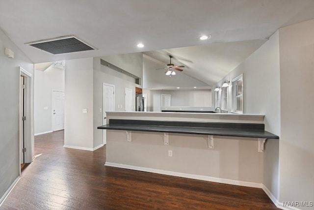 kitchen with ceiling fan, a kitchen bar, stainless steel fridge with ice dispenser, dark wood-type flooring, and vaulted ceiling