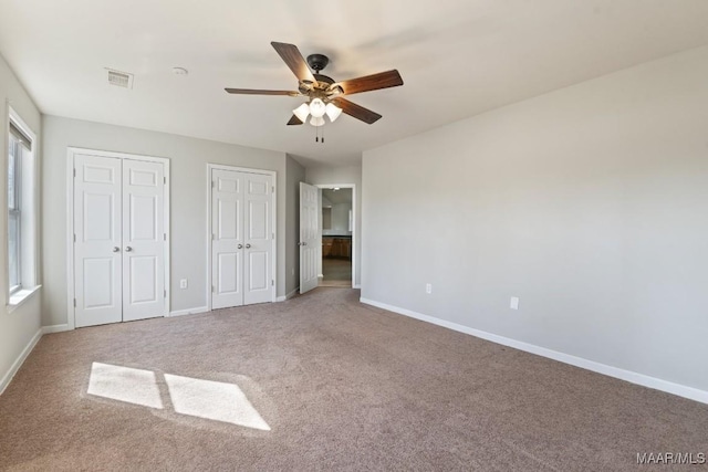 unfurnished bedroom featuring ceiling fan, carpet flooring, and two closets