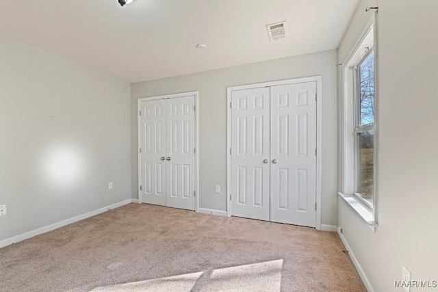 unfurnished bedroom with multiple closets and light colored carpet