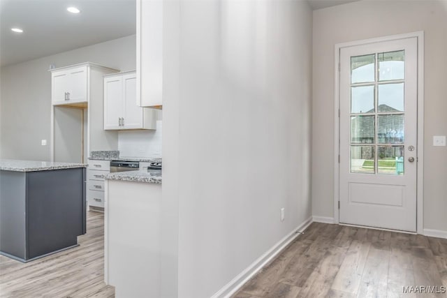 kitchen with white cabinetry, decorative backsplash, stainless steel dishwasher, light stone countertops, and light wood-type flooring