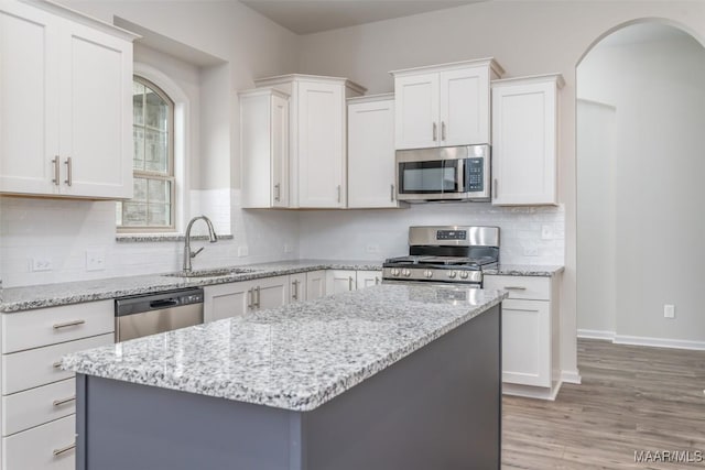 kitchen featuring appliances with stainless steel finishes, white cabinetry, sink, a center island, and light stone countertops