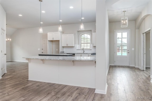 kitchen featuring a breakfast bar area, hanging light fixtures, light stone counters, white cabinets, and light wood-type flooring