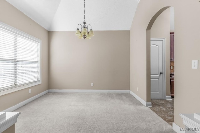 carpeted spare room with a wealth of natural light, lofted ceiling, and an inviting chandelier