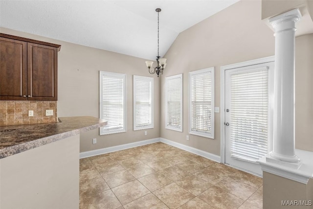 unfurnished dining area featuring a notable chandelier, vaulted ceiling, a wealth of natural light, and ornate columns