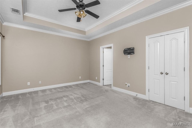 unfurnished bedroom featuring ceiling fan, light colored carpet, crown molding, and a raised ceiling