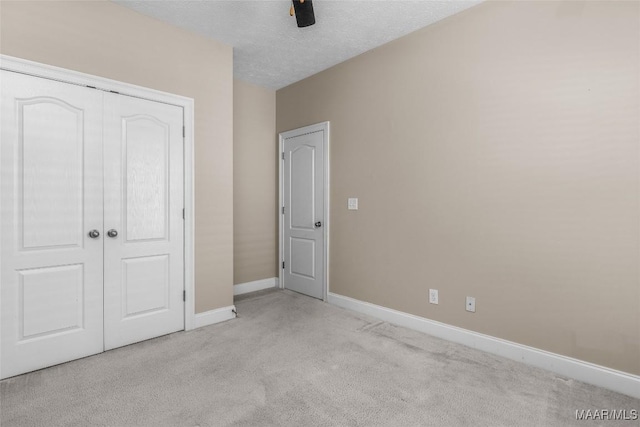 unfurnished bedroom with a textured ceiling, light colored carpet, a closet, and ceiling fan