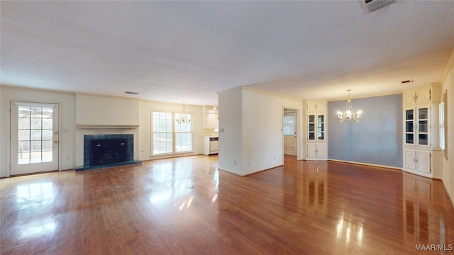 unfurnished living room with an inviting chandelier, a wealth of natural light, a tile fireplace, and a textured ceiling