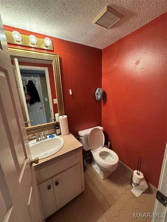 bathroom featuring tile patterned flooring, vanity, a textured ceiling, and toilet