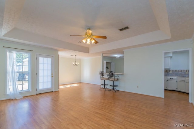 spare room featuring ceiling fan with notable chandelier, light hardwood / wood-style flooring, a textured ceiling, and a tray ceiling