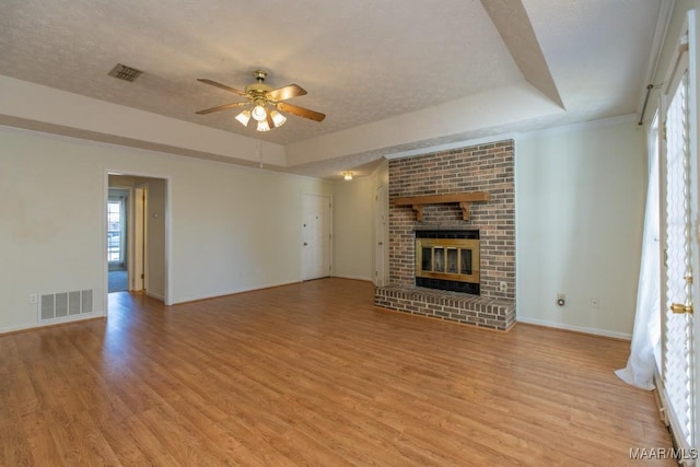 unfurnished living room with a fireplace, ceiling fan, a tray ceiling, a textured ceiling, and light hardwood / wood-style flooring