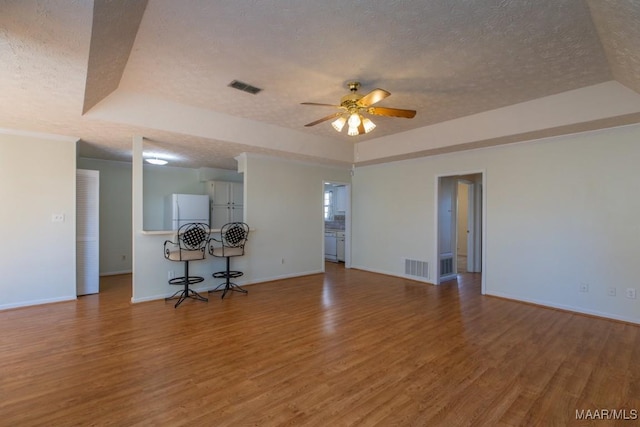 unfurnished living room with hardwood / wood-style flooring, ceiling fan, a raised ceiling, and a textured ceiling