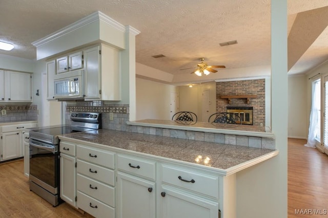 kitchen featuring stainless steel range with electric cooktop, backsplash, kitchen peninsula, a textured ceiling, and light wood-type flooring