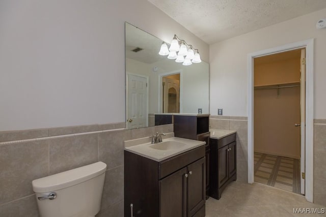 bathroom featuring tile walls, vanity, a textured ceiling, tile patterned floors, and toilet