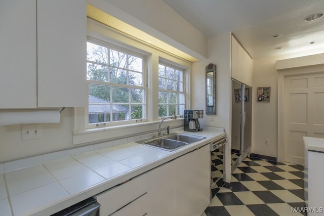 kitchen featuring tile countertops, dishwasher, sink, and white cabinets