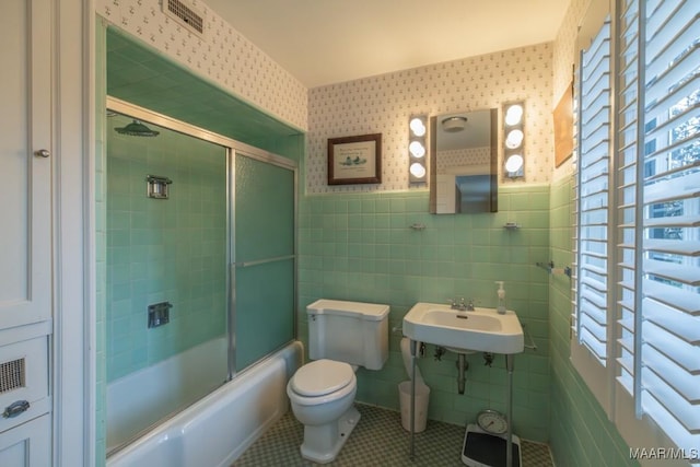 full bathroom with tile patterned floors, toilet, sink, shower / bath combination with glass door, and tile walls