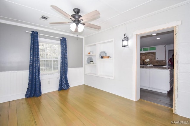 unfurnished room with built in shelves, ceiling fan, and hardwood / wood-style floors