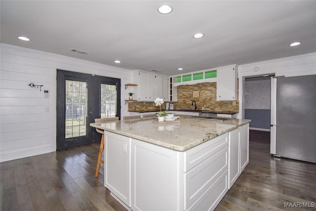 kitchen with stainless steel fridge, backsplash, a center island, light stone counters, and white cabinets