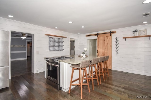 kitchen with a barn door, appliances with stainless steel finishes, a breakfast bar, and dark wood-type flooring