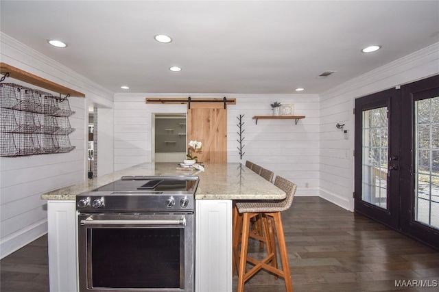 kitchen featuring wood walls, a kitchen breakfast bar, kitchen peninsula, a barn door, and high end stove