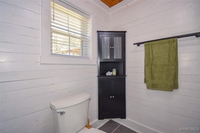 bathroom with wood walls, tile patterned floors, and toilet