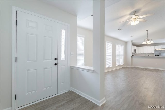 foyer featuring vaulted ceiling, wood-type flooring, and ceiling fan with notable chandelier