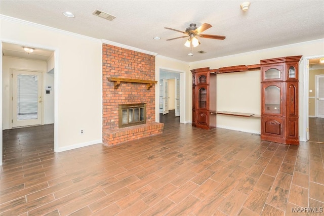 unfurnished living room featuring ceiling fan, ornamental molding, a brick fireplace, and a textured ceiling