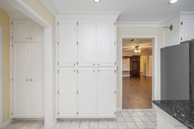 kitchen featuring white cabinetry, light tile patterned floors, ornamental molding, stainless steel fridge, and dark stone counters