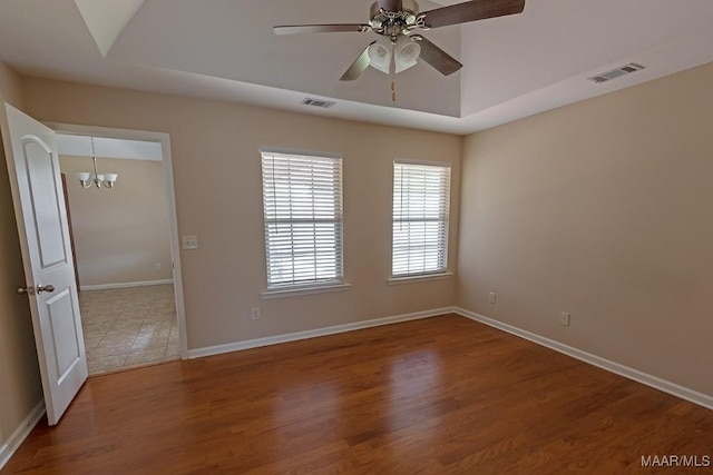 spare room featuring hardwood / wood-style flooring, ceiling fan with notable chandelier, and a tray ceiling