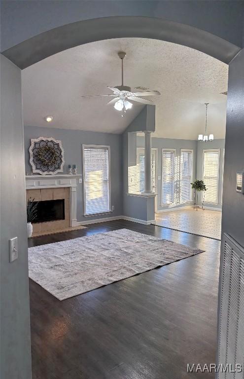 unfurnished living room featuring dark wood-type flooring, vaulted ceiling, a textured ceiling, a tile fireplace, and ceiling fan