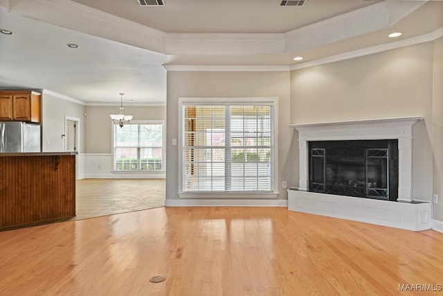 unfurnished living room with a raised ceiling, ornamental molding, a chandelier, and light hardwood / wood-style flooring