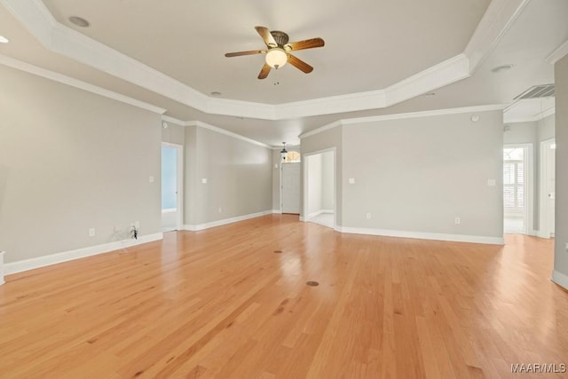 empty room with a raised ceiling, ornamental molding, and light wood-type flooring