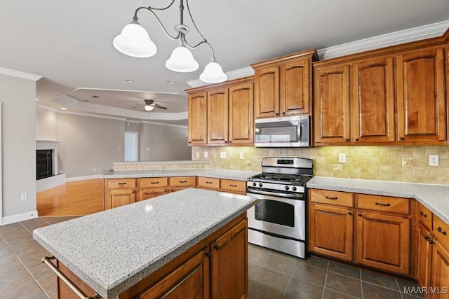 kitchen featuring ceiling fan, stainless steel appliances, a center island, ornamental molding, and decorative light fixtures