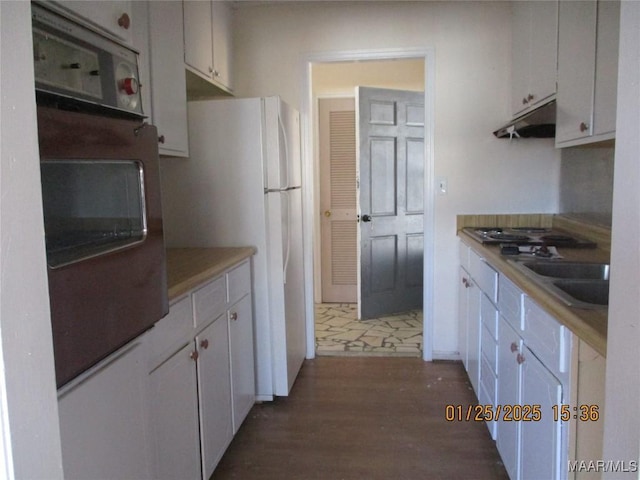 kitchen featuring white refrigerator, gas stovetop, sink, and white cabinets