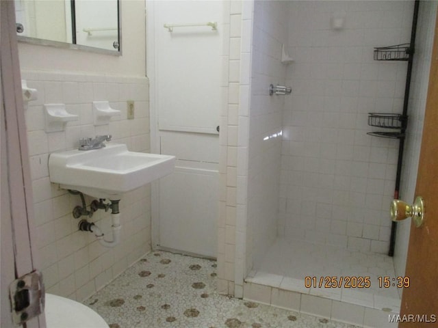 bathroom featuring a tile shower, sink, tile walls, tile patterned flooring, and toilet