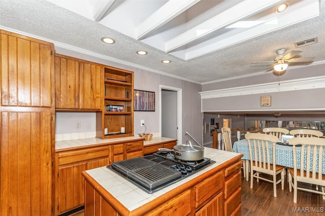 kitchen with tile countertops, black gas cooktop, a center island, crown molding, and a textured ceiling