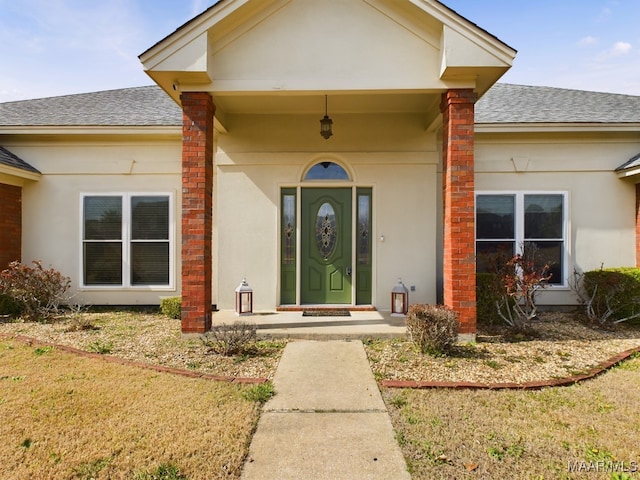 entrance to property featuring roof with shingles, a yard, and stucco siding