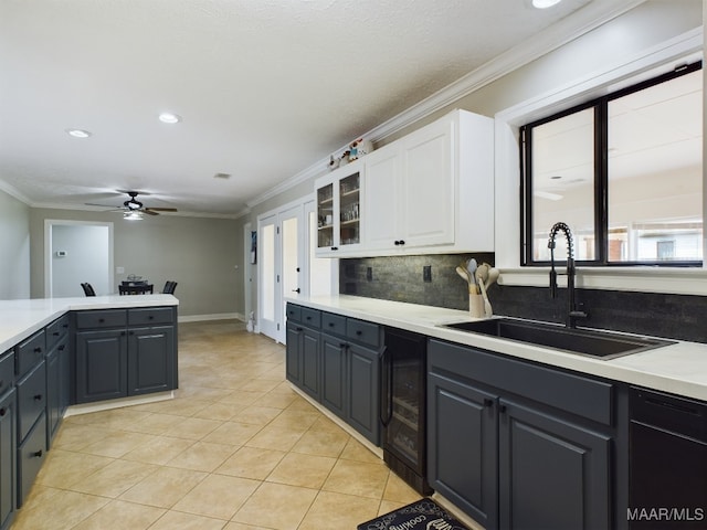 kitchen featuring white cabinets, ornamental molding, glass insert cabinets, light countertops, and a sink