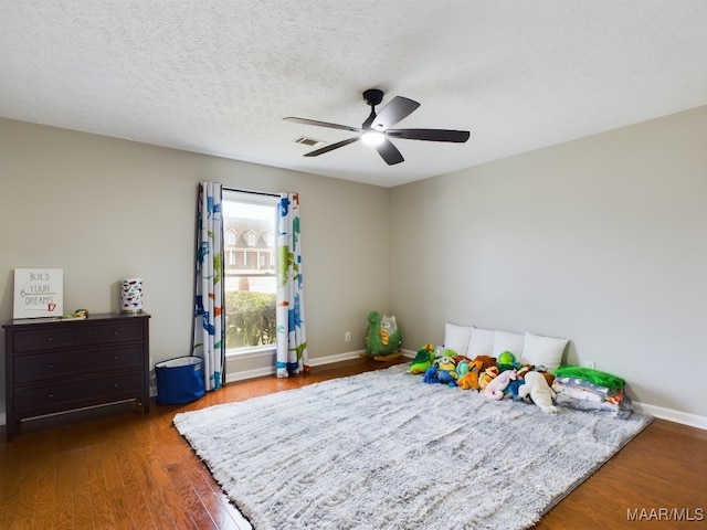 bedroom with baseboards, visible vents, a ceiling fan, dark wood-style floors, and a textured ceiling