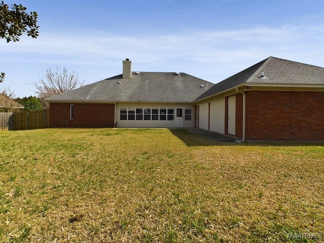 rear view of property with brick siding, fence, a yard, roof with shingles, and a chimney