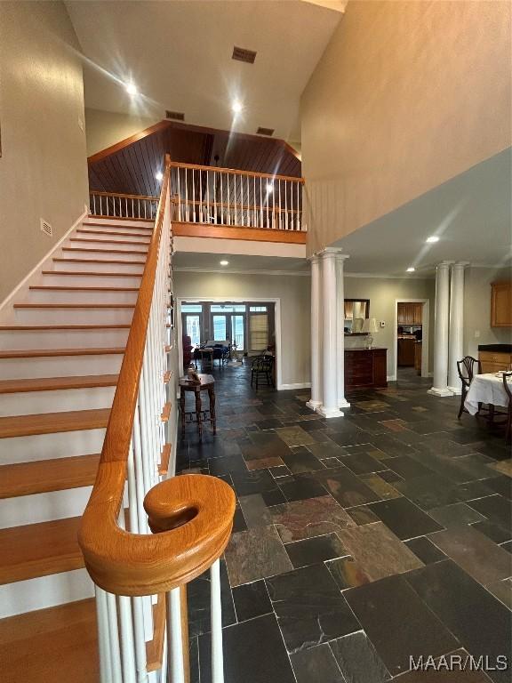 stairs with stone tile flooring, baseboards, decorative columns, and a towering ceiling
