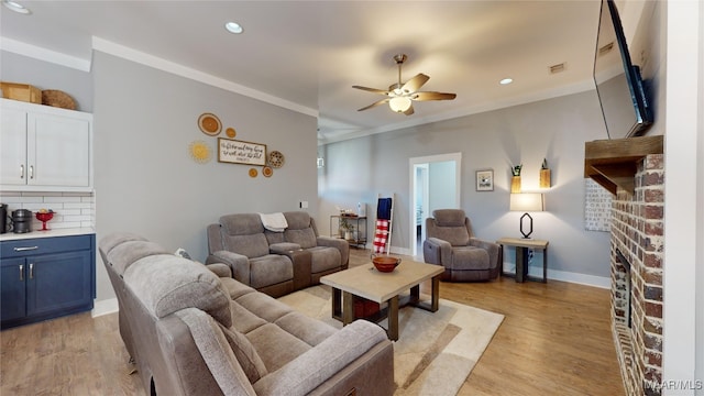 living room featuring a brick fireplace, crown molding, ceiling fan, and light wood-type flooring