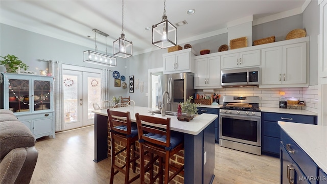 kitchen featuring appliances with stainless steel finishes, backsplash, hanging light fixtures, a center island with sink, and french doors