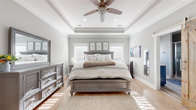 bedroom with a barn door, light wood-type flooring, ceiling fan, and a tray ceiling