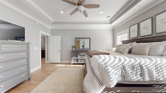 bedroom with ceiling fan, a tray ceiling, and light hardwood / wood-style flooring