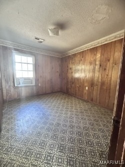 unfurnished room with crown molding, a textured ceiling, and wooden walls