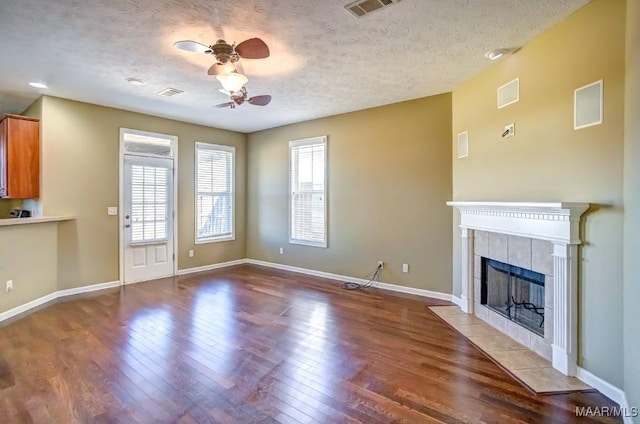 unfurnished living room with a tiled fireplace, wood-type flooring, ceiling fan, and a textured ceiling