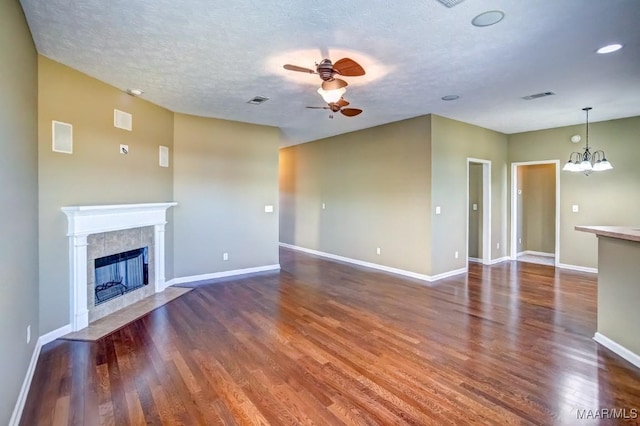 unfurnished living room with a tiled fireplace, ceiling fan with notable chandelier, a textured ceiling, and dark hardwood / wood-style flooring