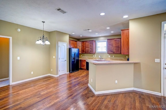 kitchen with black fridge, dark hardwood / wood-style floors, an inviting chandelier, and kitchen peninsula