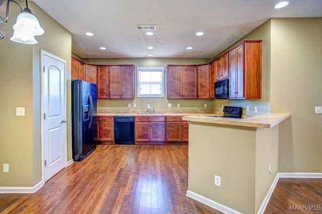 kitchen with sink, dark wood-type flooring, black appliances, decorative light fixtures, and kitchen peninsula